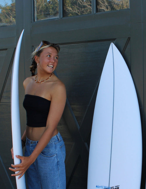 Talia Swindal holding a surfboard in front of a garage door