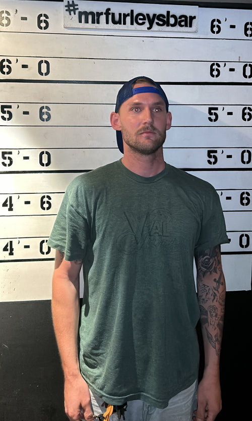 Joey Mailes wearing a green "Val Surf t-shirt standing in front of a height chart at MRFurley's Bar