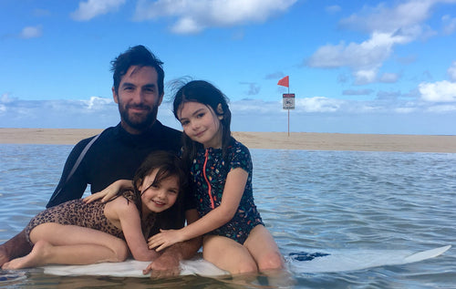 Jordan Tappis and his daughters on a surfboard together in the ocean