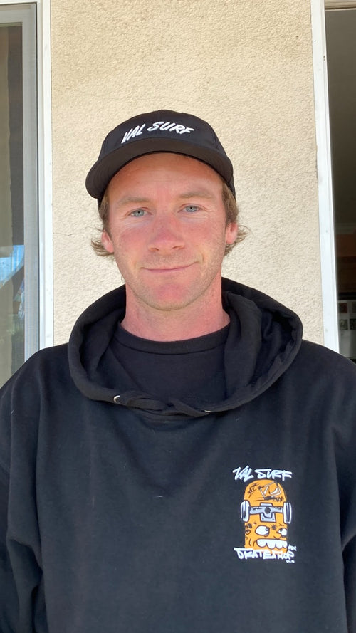 Austin Barks standing in front of a wall wearing a "Val Surf" hat and "Val Surf" hooded sweatshirt