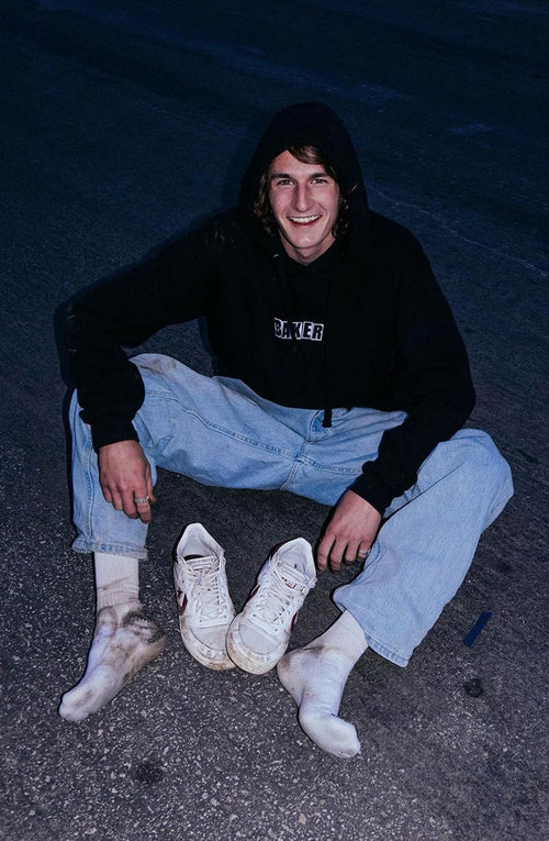 Brody Jacobson sitting on the ground with his shoes off wearing a "Baker" hooded sweatshirt