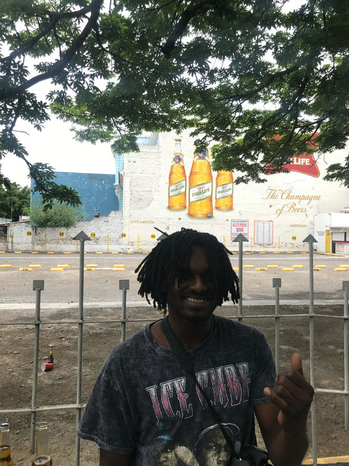 Cyril Jackson throwing a "Shaka" in front of a fence while wearing an "Ice Cube" shirt