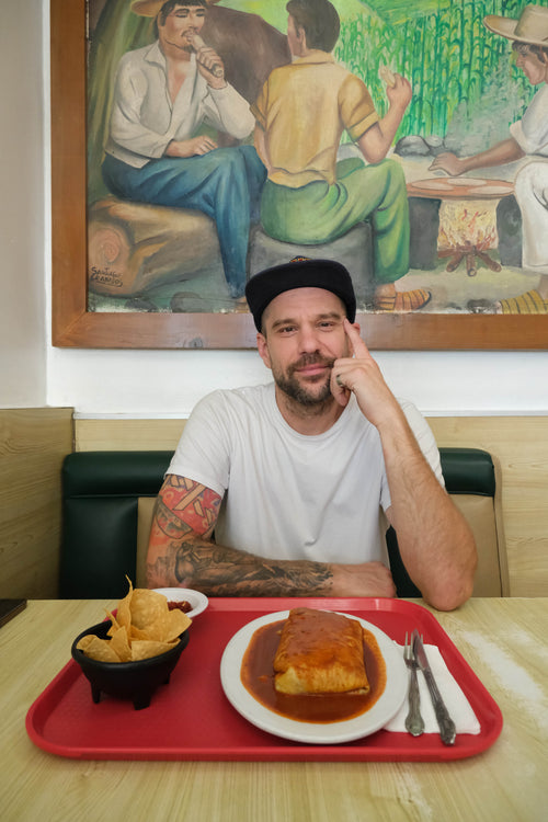 Casey Morrissey sitting at a table with a tray of food in a restaurant setting, artwork on the wall behind him