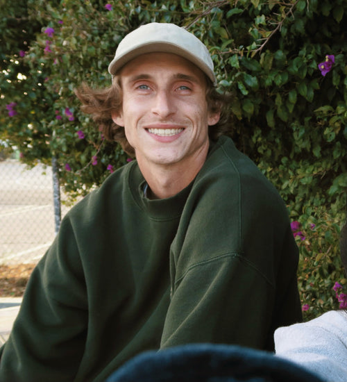 Tony smiling in front of a tree while wearing a white hat and green crewneck sweatshirt