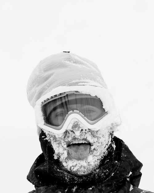 Garrett Warnick with snow all over his face sticking his tongue out, and wearing snow goggles and a beanie