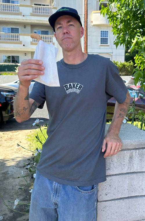 Andrew Reynolds wearing a gray 'Baker' t-shirt holding a churro at Val Surf