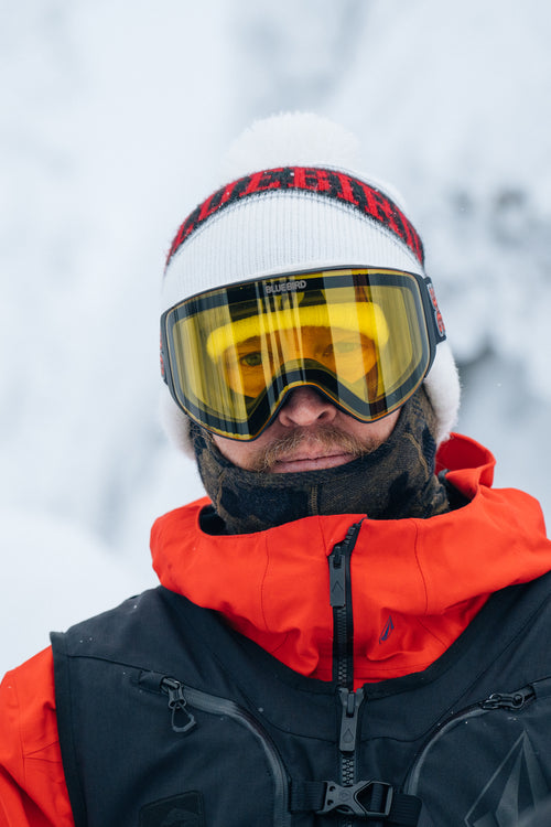 Kurt Wastell wearing a white knit cap with red accents, yellow goggles, and a black and orange jacket in a snowy background.