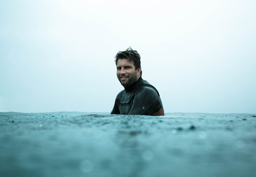 Anthony Petruso in a wetsuit sitting on his surfboard in the ocean