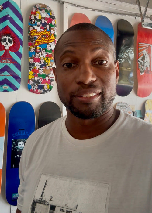 Steve Kindle standing in front of a wall with colorful skateboard decks