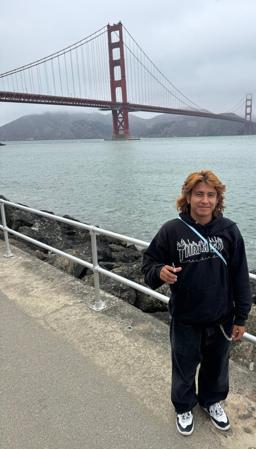 Gio  Becerril standing in front of the Golden Gate Bridge wearing a Thrasher hooded sweatshirt