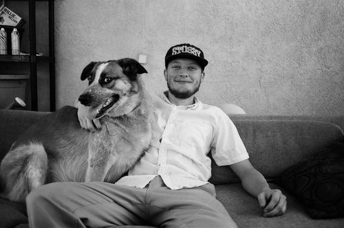 Kevin Terpening sitting on a couch holding his dog while wearing a "Stussy" hat