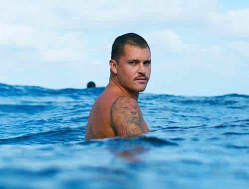 Lyon Herron sitting on his surfboard in the ocean in heaven