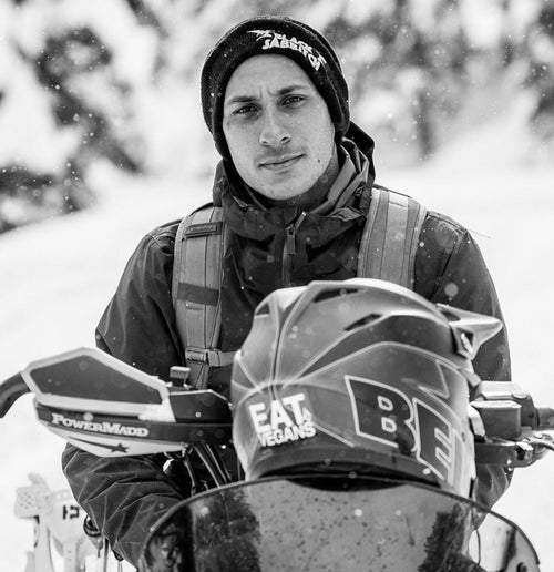 A black and white photo of Scott Blum sitting on a snowmobile wearing a Black Sabbath beanie