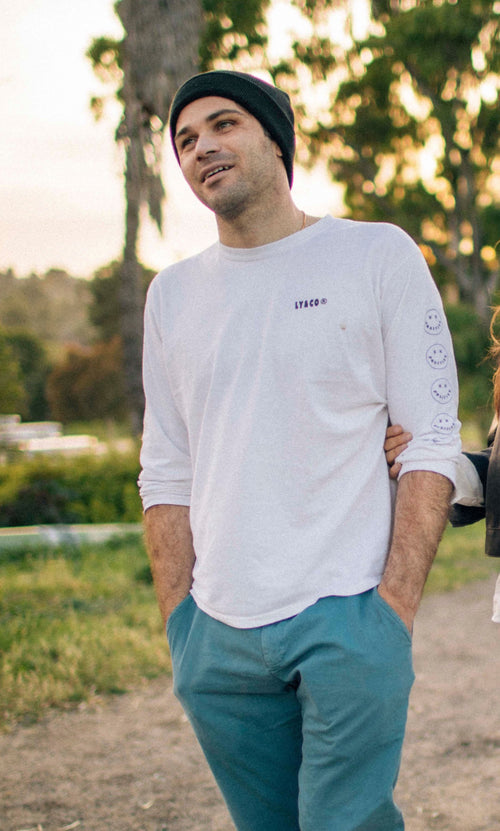 Colton Sarlo wearing a white long-sleeve shirt with text and teal pants standing outdoors