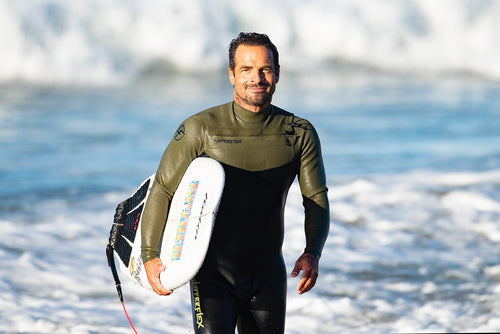 Yves Bight getting our of the ocean while carrying his surfboard still in his wetsuit