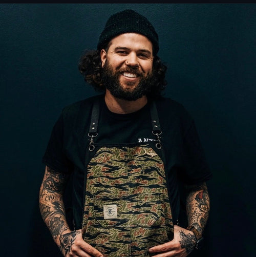 Mason Aguirre wearing a camouflage bib over a black shirt against a dark background