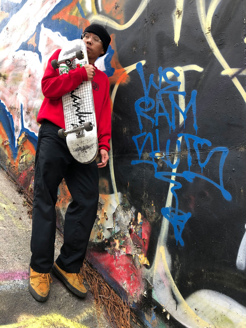 Ram Pong standing in front of a graffiti wall while holding his skateboard
