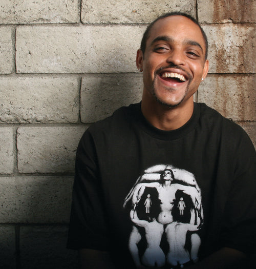 Jeron Wilson wearing a black GIRL Tishirt with a graphic design, sitting against a concrete brick wall