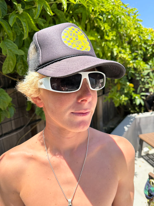 Tosh Webb wearing a "Val Surf" cap and sunglasses with an ivy plant background