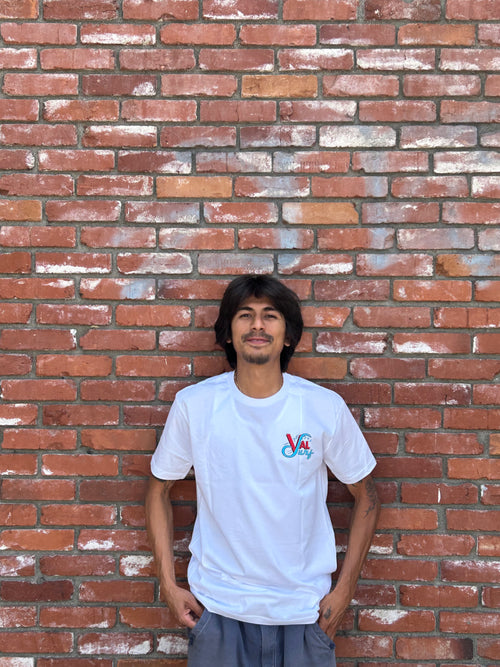 Waldo Diaz wearing a white "Val SUrf" t-shirt against the brick wall at Val Surf