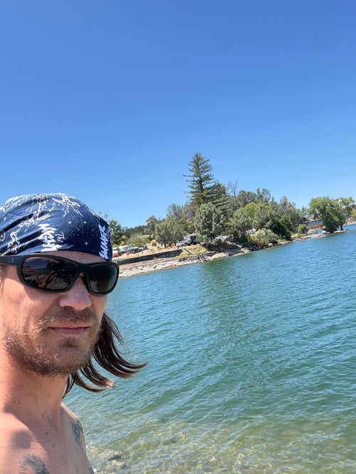Zack Krull with sunglasses and bandana by a lake with trees in the background